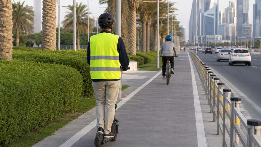 An electric scooter rider wearing a helmet and safety vest on a designated track in Doha Qatar